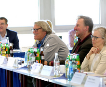 Teilnehmende sitzen an Tischen und hören zu.