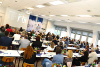 Ein Redner steht vorne im Saal am Pult, das Publikum verfolgt seinen Vortrag.