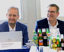Zwei Männer am Konferenztisch im Gespräch, umgeben von Getränken und Unterlagen.