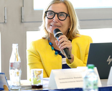 Eine Frau im gelben Blazer spricht ins Mikrofon während der Veranstaltung.