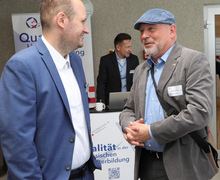 Zwei Männer im Gespräch mit einem weiteren Mann am Infostand.
