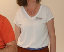 Frau mit Namensschild in weißem Shirt lächelt und steht an einem Tisch.