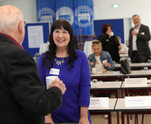 Frau im Gespräch mit einem älteren Mann; beide stehen in einem Veranstaltungsraum.