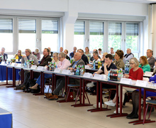 Frontale Perspektive auf den Saal mit voll besetzten Tischen und aufmerksamem Publikum.