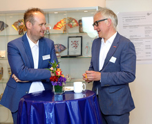 Zwei Männer im Gespräch an einem Stehtisch mit Blumen und Wasserflaschen.