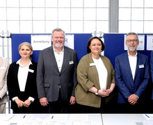 Die Beschäftigten der Geschäftsstelle posieren vor einem Infoposter für ein Gruppenfoto.