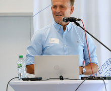 Redner mit Laptop spricht am Pult.