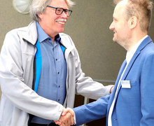 Zwei Männer begrüßen sich per Handschlag und lachen.